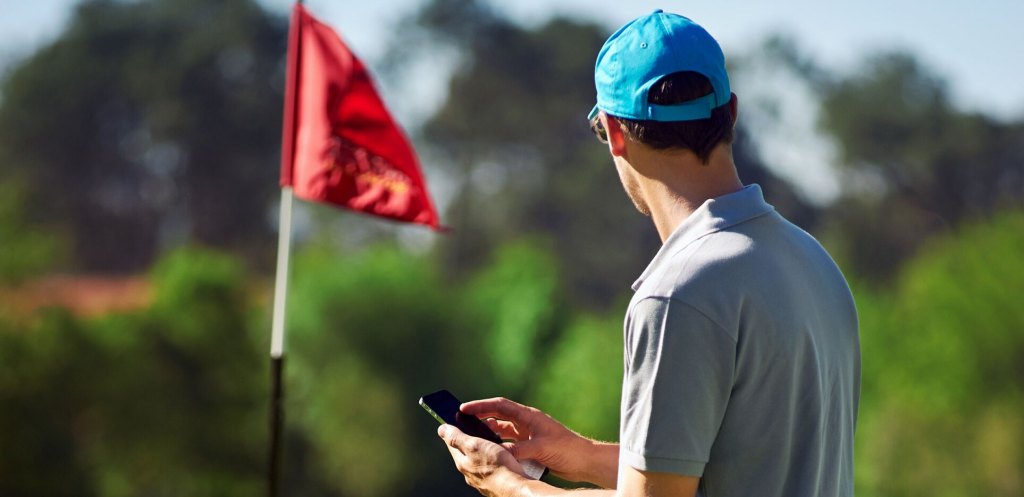 Golfer with mobile phone on golf course with red flag in distance 